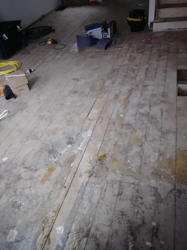 A dirty wooden floor in a room with stairs.