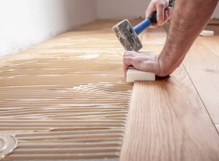 A man is applying glue to a wooden floor with a hammer and sponge.
