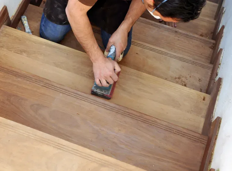 A man is sanding a wooden staircase with a sander